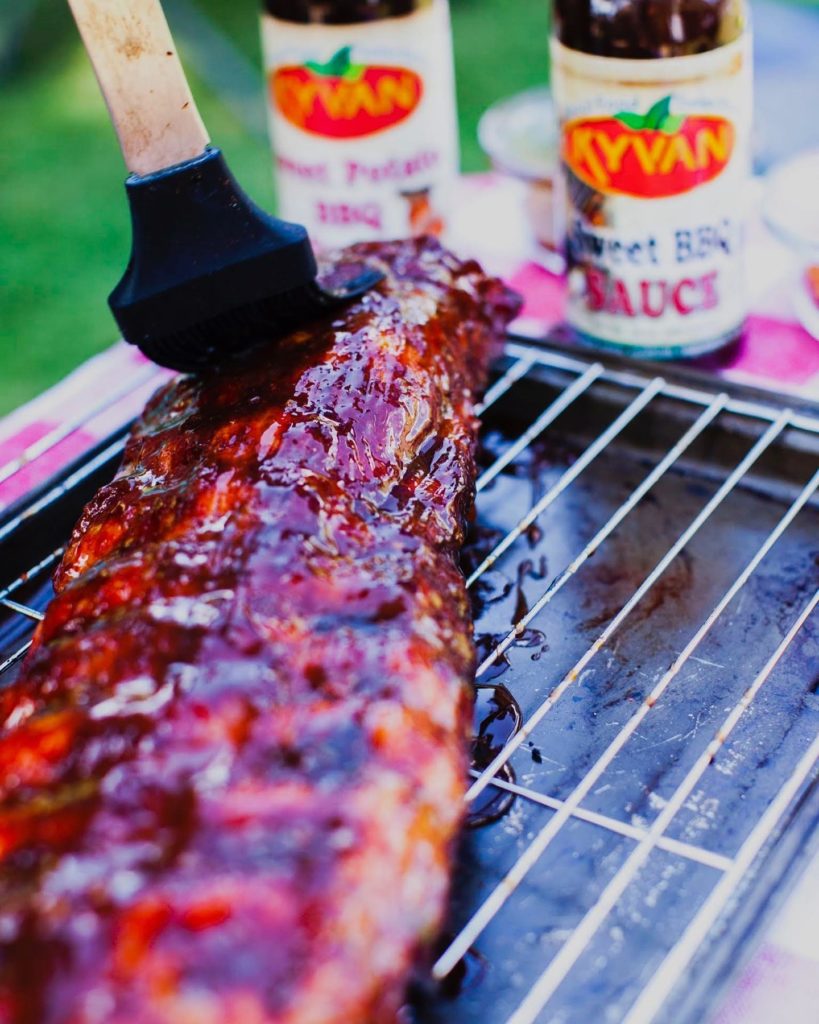Grilled Ribs being slathered with Kyvan Foods Sweet BBQ Sauce