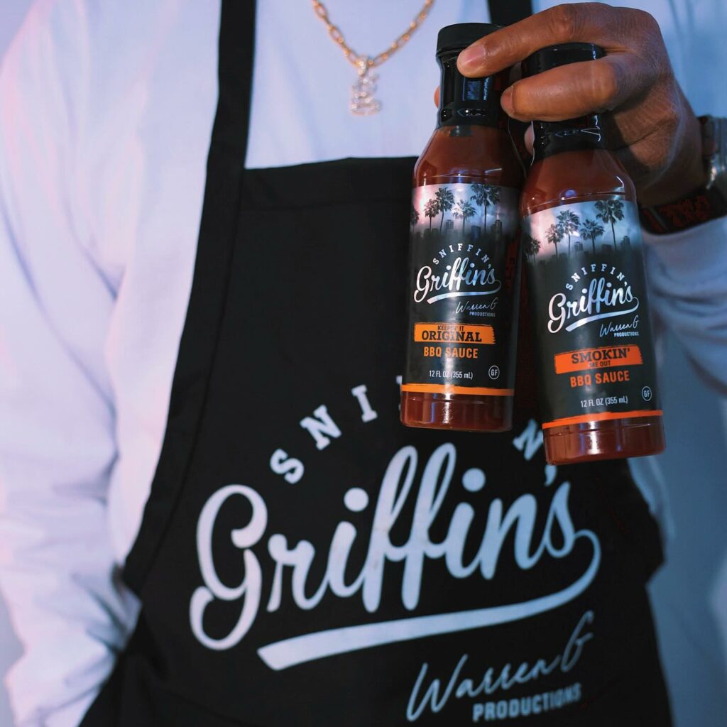 Warren G holding two bottles of his Sniffin' Griffins BBQ Sauce