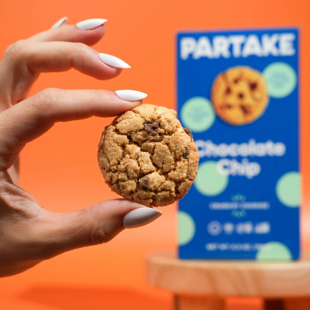 a woman holding a Partake chocolate chip cookie in front of the box