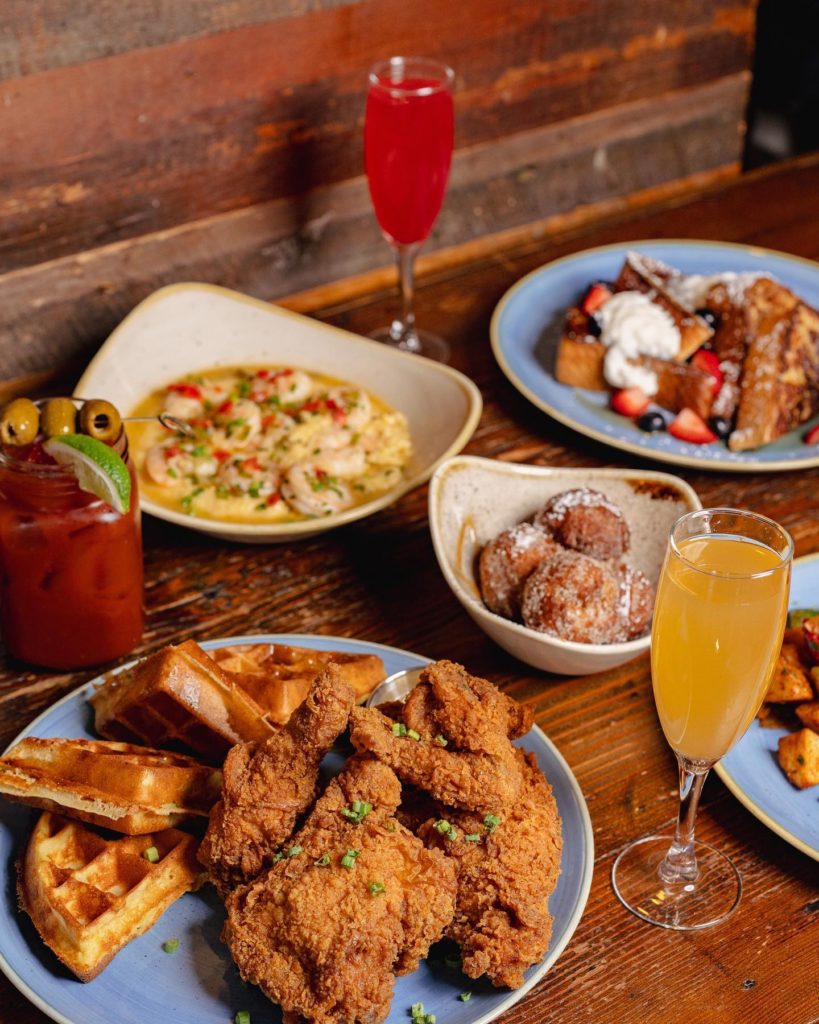 Table full of Brunch selections from Arlington's Hen Quarter with chicken and waffles, french toast, shrimp and grits and a bloody mary