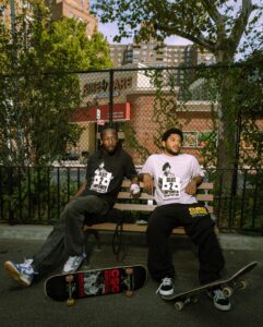 Two young men on a bench in the park with their skateboards rocking crenshaw skate club gear